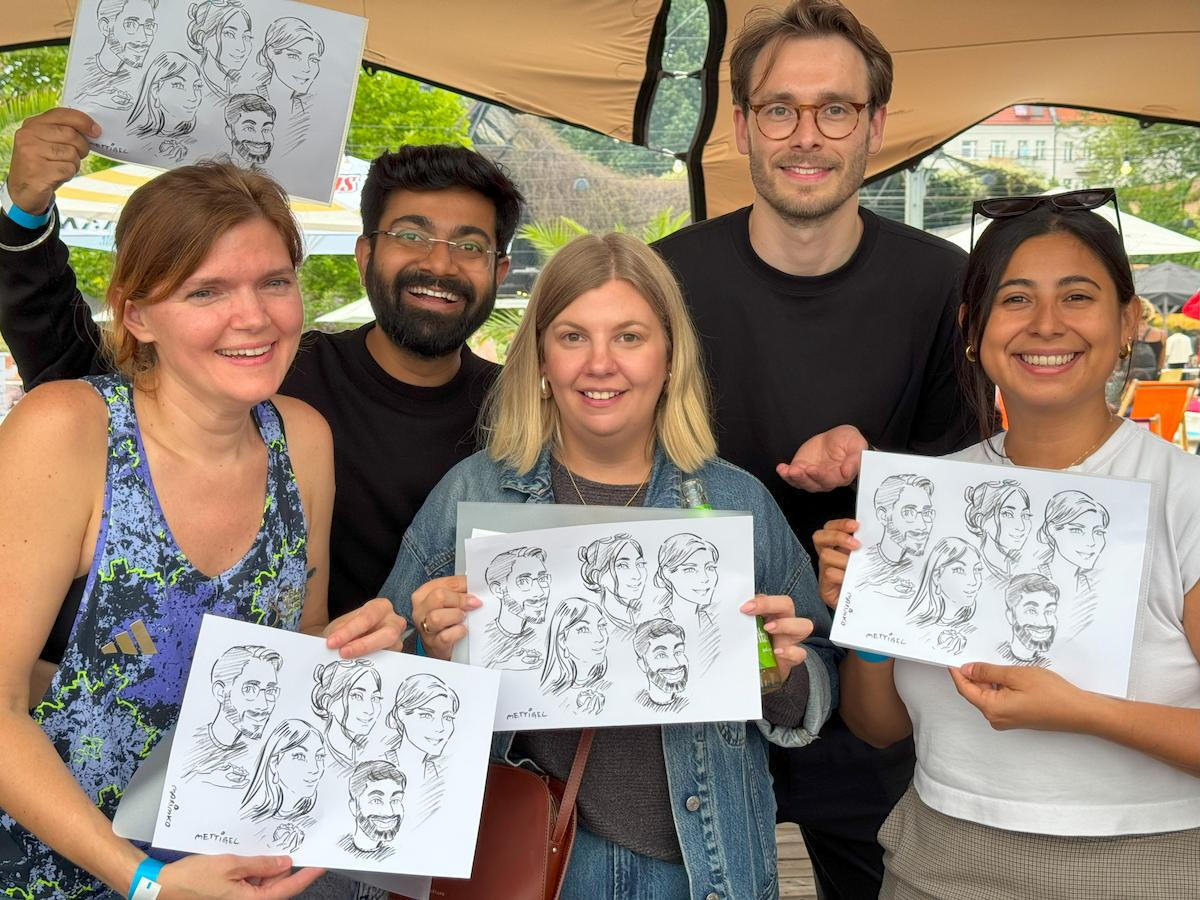 企業のパーティーで、描いてもらったばかりの似顔絵を手に笑顔を見せる参加者のグループ。